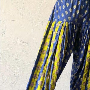 Op de afbeelding: Blauwe en gele gepatroneerde broek met een geplooide tailleband en wijde pijpen. De broek heeft een bloemenprint en strepen.