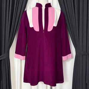 May include: A vintage purple dress with a high collar and three-quarter sleeves. The dress features white and pink color-block detailing on the shoulders and cuffs. The dress is displayed on a mannequin.