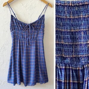 Puede incluir: Un vestido mini de cuadros azules y rosas con tirantes finos y un lazo en el escote. El vestido tiene un corpi&ntilde;o fruncido y una falda fluida.