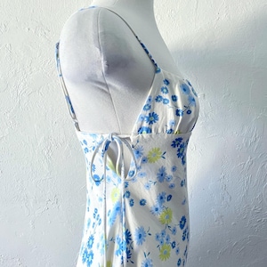 May include: A white sleeveless dress with a blue and yellow floral print. The dress has a tie at the back and a square neckline.