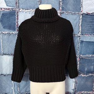 Puede incluir: Un su&eacute;ter negro de cuello alto de punto grueso. El su&eacute;ter tiene cuello, pu&ntilde;os y dobladillo acanalados. El cuerpo del su&eacute;ter tiene un dise&ntilde;o de punto abierto texturizado. Las mangas son largas y el su&eacute;ter es corto.