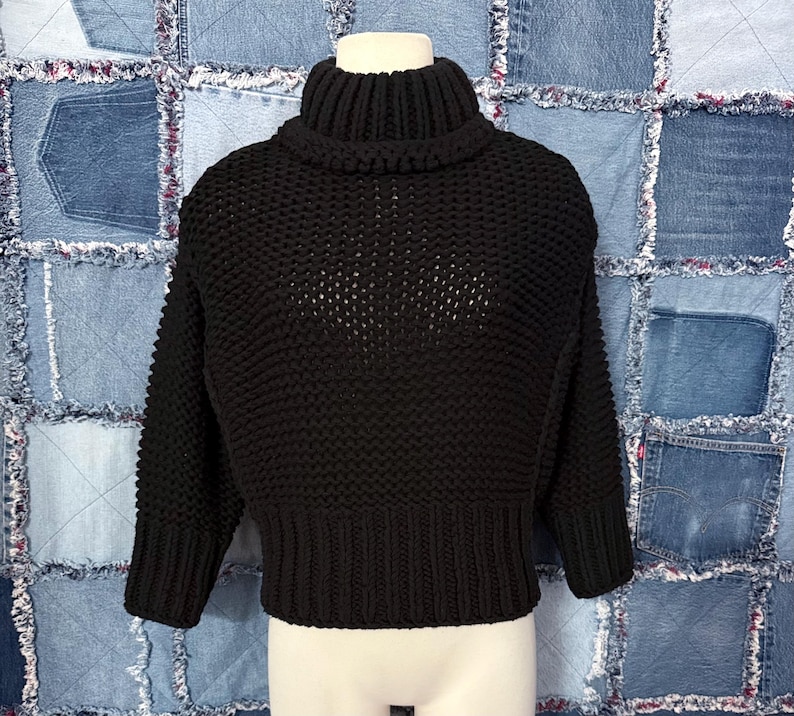 Puede incluir: Un su&eacute;ter negro de cuello alto de punto grueso. El su&eacute;ter tiene cuello, pu&ntilde;os y dobladillo acanalados. El cuerpo del su&eacute;ter tiene un dise&ntilde;o de punto abierto texturizado. Las mangas son largas y el su&eacute;ter es corto.