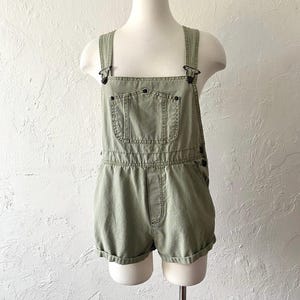 May include: A pair of green denim overalls with adjustable straps and a single front pocket. The overalls have a relaxed fit and are made of a soft, comfortable fabric.