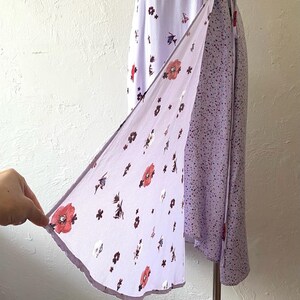 May include: A lavender wrap dress with a floral print and a tie closure. The dress has a shorter hem in the front and a longer hem in the back.