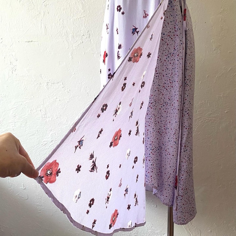 May include: A lavender wrap dress with a floral print and a tie closure. The dress has a shorter hem in the front and a longer hem in the back.