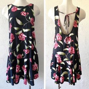 May include: A black sleeveless dress with a floral print of pink roses and green leaves. The dress has a tie at the back of the neck and a ruffled hem.