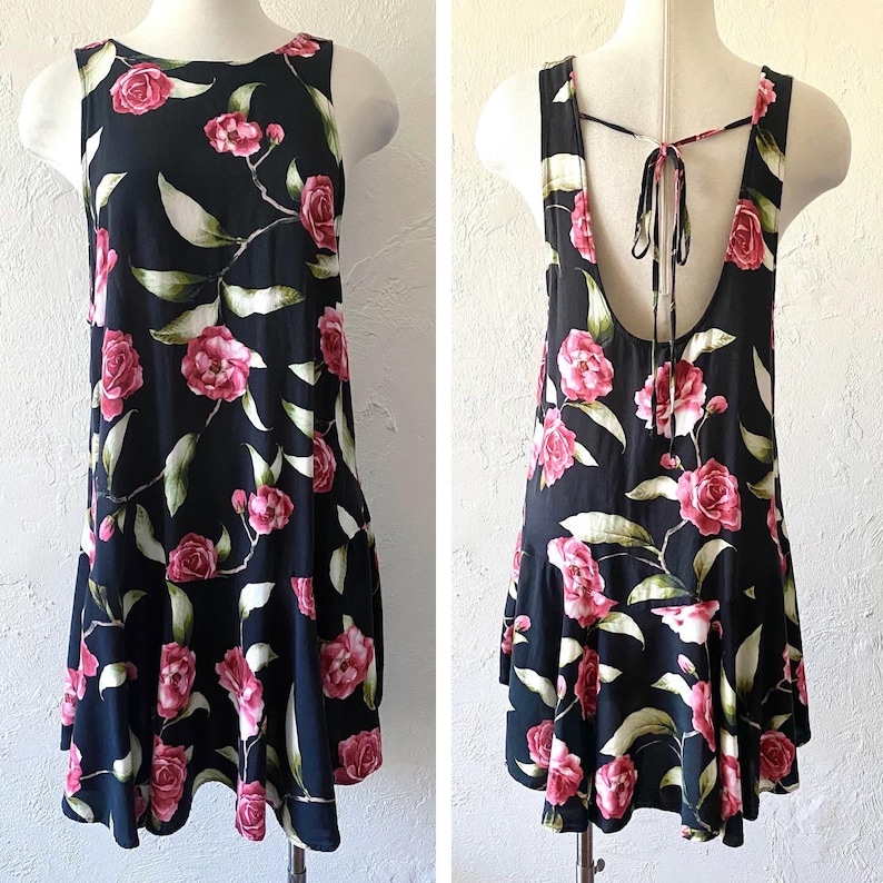 May include: A black sleeveless dress with a floral print of pink roses and green leaves. The dress has a tie at the back of the neck and a ruffled hem.