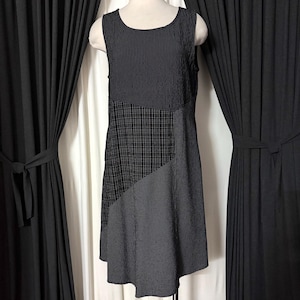 May include: Sleeveless black dress with a patchwork design. The top section features vertical stripes, the middle has a grid pattern, and the bottom has a small polka dot pattern. The dress is displayed on a mannequin.