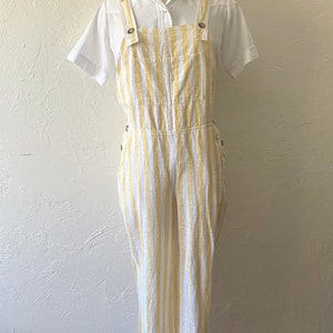 May include: White and yellow striped linen overalls with a white collared shirt.