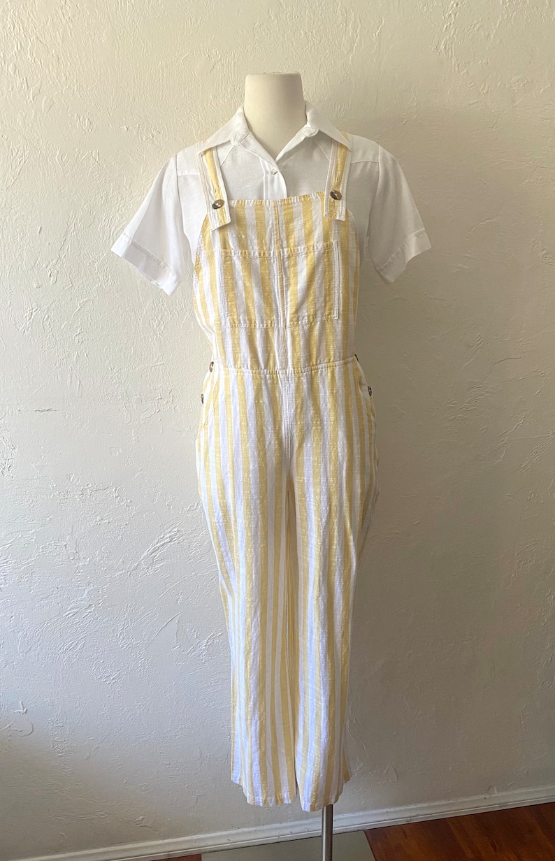 May include: White and yellow striped linen overalls with a white collared shirt.
