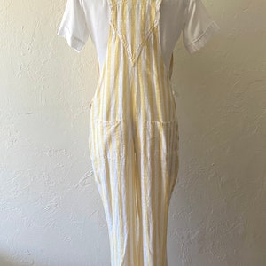 May include: White and yellow striped linen overalls with a V-neck and two front pockets.