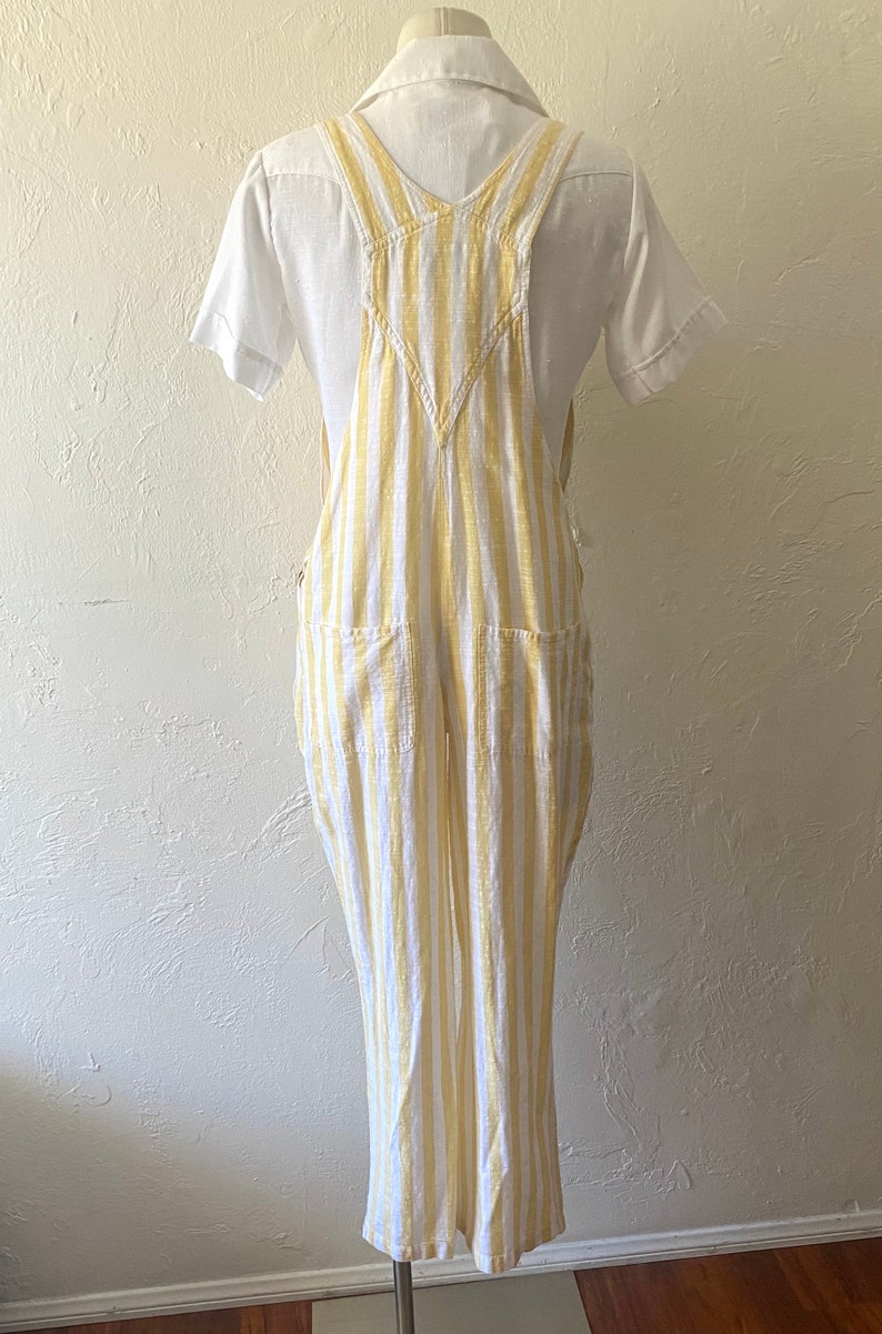 May include: White and yellow striped linen overalls with a V-neck and two front pockets.