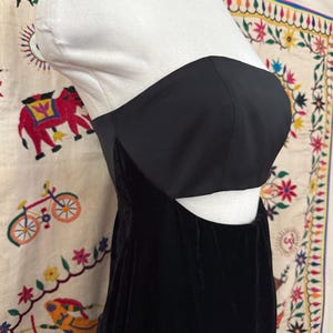 Może przedstawiać: Czarna, bez ramiączek, aksamitna sukienka z wycięciem w talii.