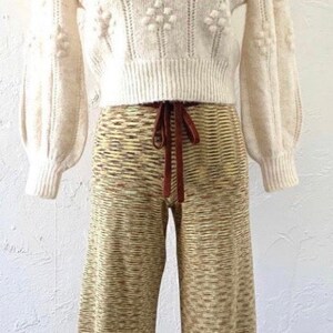 May include: A white knitted sweater with a ruffled collar and a brown and beige knitted wide-leg pant.