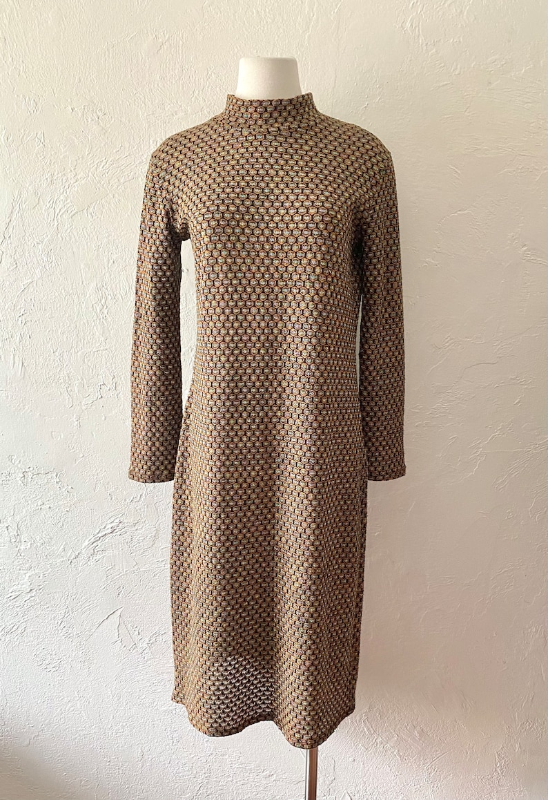 May include: A long-sleeved dress with a high mock neck. The dress is made of a brown and beige fabric with a geometric pattern.