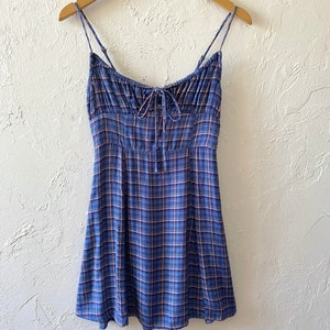 Puede incluir: Un vestido mini de cuadros azules y blancos con tirantes finos y un lazo en el escote.