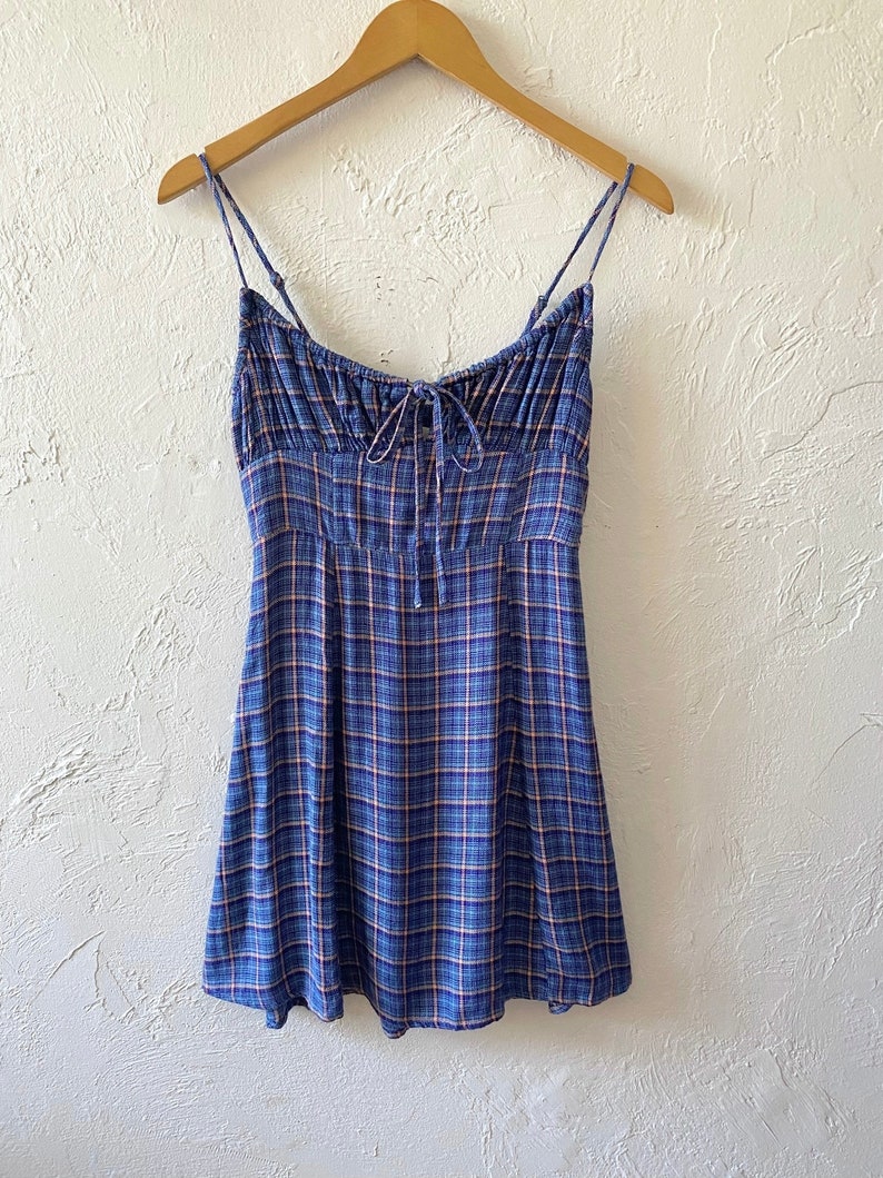Puede incluir: Un vestido mini de cuadros azules y blancos con tirantes finos y un lazo en el escote.