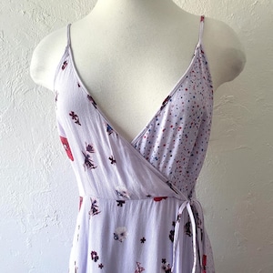 May include: A lavender wrap dress with a floral print featuring red, white, and blue flowers. The dress has a V-neckline and adjustable straps.