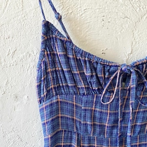 Puede incluir: Un vestido sin mangas de cuadros azules y naranjas con un lazo en el escote.