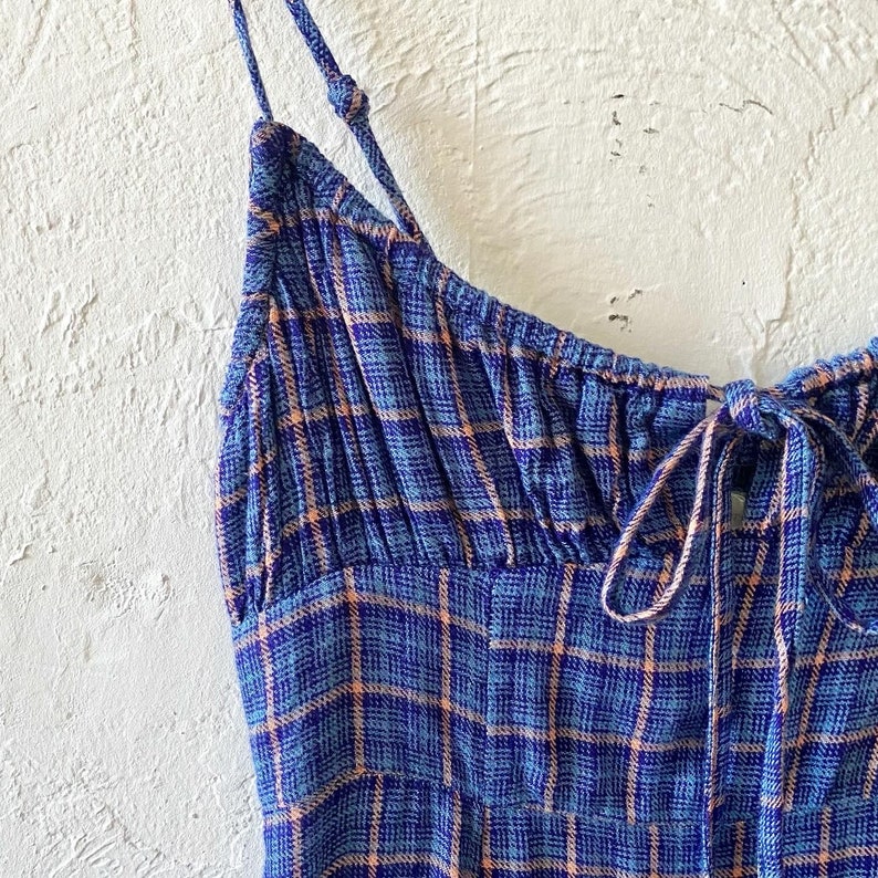 Puede incluir: Un vestido sin mangas de cuadros azules y naranjas con un lazo en el escote.