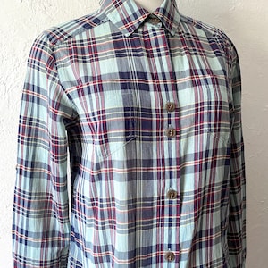Pode incluir: Uma camisa de manga comprida com botões e um padrão xadrez em tons de azul, vermelho e branco.