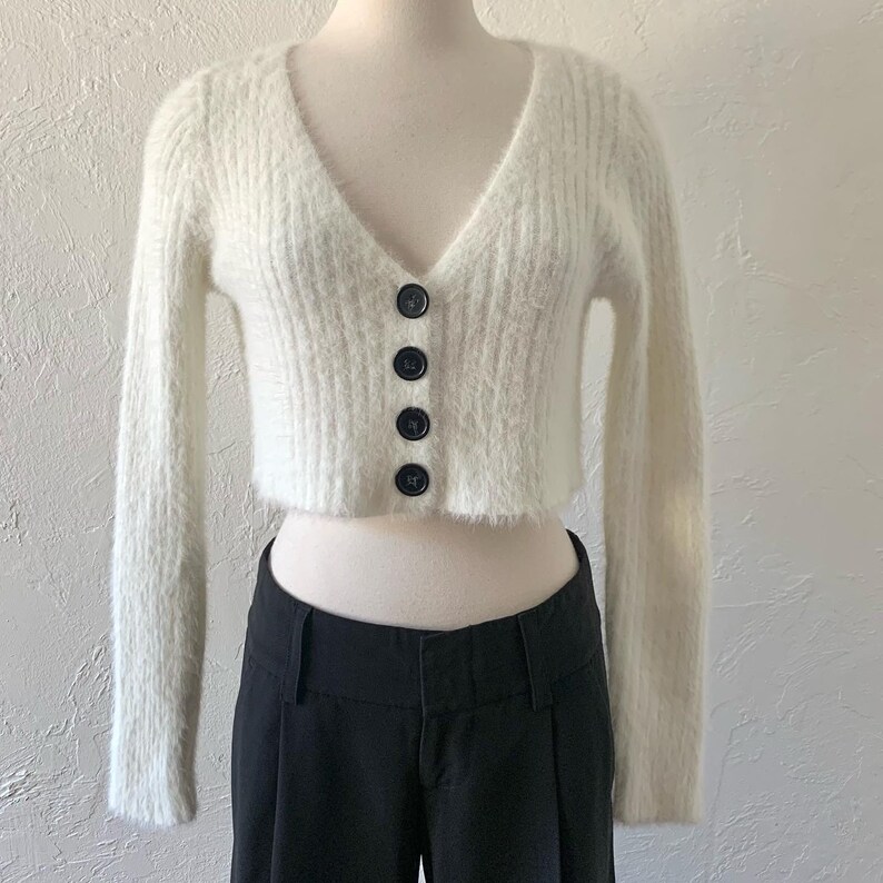 Peut inclure: Un cardigan blanc en fourrure, court, &agrave; col en V et fermeture boutonn&eacute;e. Le cardigan a des manches longues et une texture c&ocirc;tel&eacute;e.