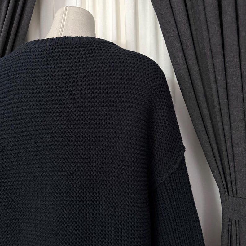 May include: A dark navy blue knit sweater with a crew neck. The sweater has a textured, open weave design. The garment is displayed on a mannequin, with a dark curtain in the background.