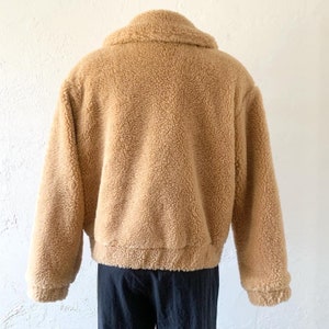 K&ouml;nnte beinhalten: Eine braune Teddyfelljacke mit Rei&szlig;verschluss. Die Jacke hat einen Kragen und lange &Auml;rmel.
