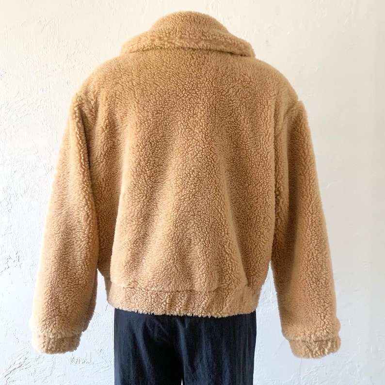 K&ouml;nnte beinhalten: Eine braune Teddyfelljacke mit Rei&szlig;verschluss. Die Jacke hat einen Kragen und lange &Auml;rmel.