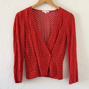 May include: A red wrap top with a white floral print and long sleeves.