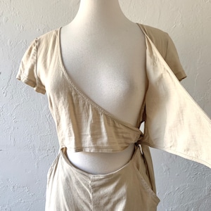 May include: A beige jumpsuit with a short-sleeved, wrap-style top and a cutout detail at the waist. The top has a tie detail at the side.