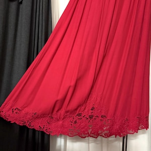 May include: A bright red dress with a flowing design. The hemline has a delicate floral cut-out pattern. The fabric drapes elegantly, highlighting the dress's texture and colour.
