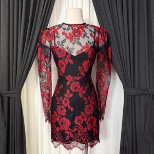 Może przedstawiać: Czarna mini sukienka z czerwoną kwiatową koronkową nakładką. Sukienka ma długie rękawy, okrągły dekolt i falisty dół. Kwiatowy wzór jest widoczny na rękawach i gorsecie, tworząc uderzający kontrast.