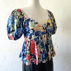 Puede incluir: Una blusa de estampado floral con escote de coraz&oacute;n y mangas abullonadas. La blusa tiene un corpi&ntilde;o ajustado y un dobladillo de p&eacute;plum con volantes.