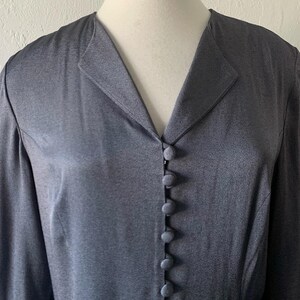 May include: A long-sleeved, dark gray button-up shirt with a v-neck collar.
