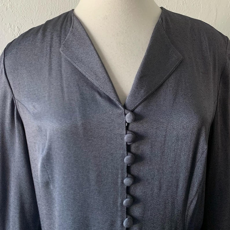 May include: A long-sleeved, dark gray button-up shirt with a v-neck collar.