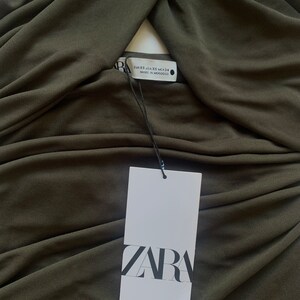 Puede incluir: Un top sin mangas de color verde oscuro, el&aacute;stico, con un escote retorcido. El top tiene una etiqueta blanca con la palabra "ZARA" impresa en ella. La etiqueta tambi&eacute;n incluye la informaci&oacute;n de la talla: EUR XS, USA XS, MEX 24, MADE IN MOROCCO.