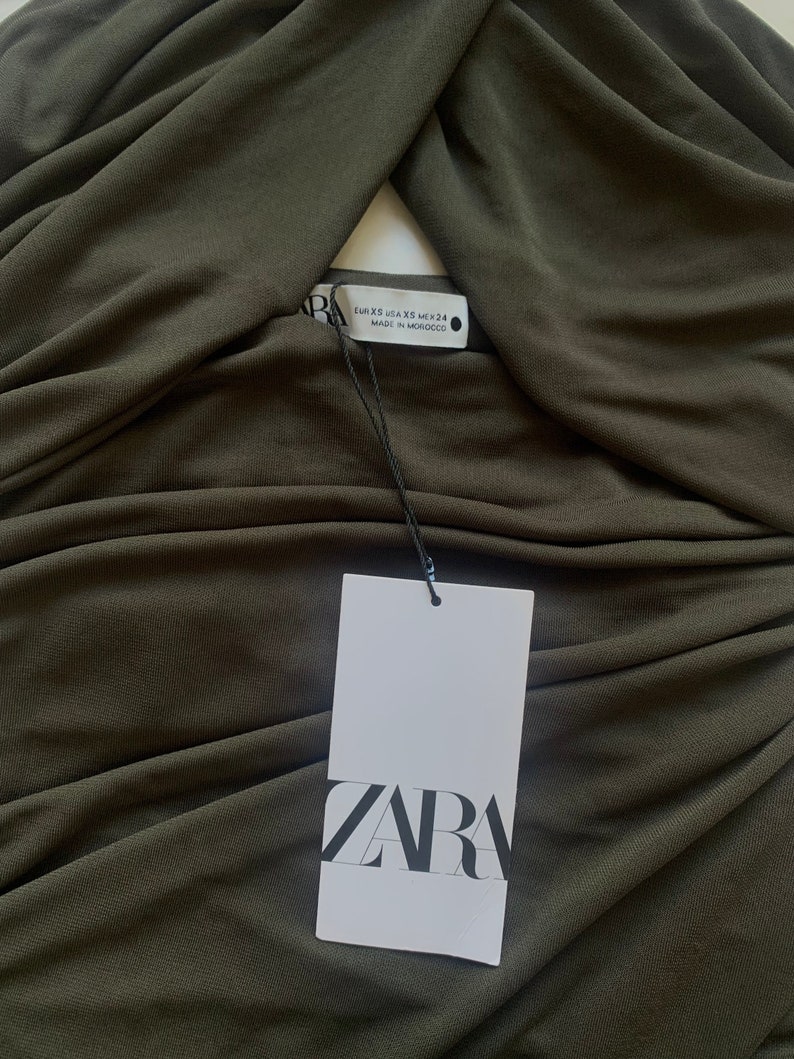 Puede incluir: Un top sin mangas de color verde oscuro, el&aacute;stico, con un escote retorcido. El top tiene una etiqueta blanca con la palabra "ZARA" impresa en ella. La etiqueta tambi&eacute;n incluye la informaci&oacute;n de la talla: EUR XS, USA XS, MEX 24, MADE IN MOROCCO.