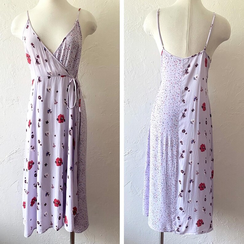 May include: A lavender midi dress with a floral print and a wrap style bodice. The dress has a tie at the waist and a spaghetti strap design.