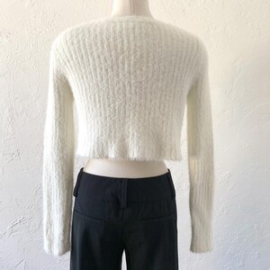 Peut inclure: Gilet en maille blanc duveteux &agrave; manches longues et coupe courte. Le gilet a une texture c&ocirc;tel&eacute;e et un ourlet l&eacute;g&egrave;rement effiloch&eacute;.