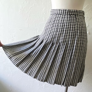 May include: A black and white houndstooth pleated skirt. The skirt is knee-length and has a flared silhouette.