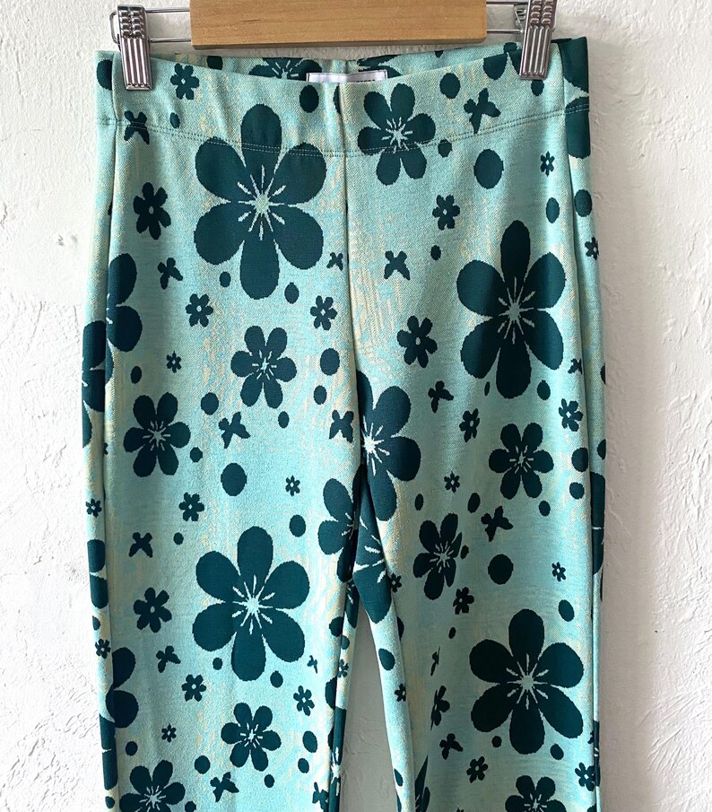 K&ouml;nnte beinhalten: Eine blaue Hose mit gr&uuml;nem Blumenmuster. Die Hose hat eine hohe Taille und ein gerades Bein.