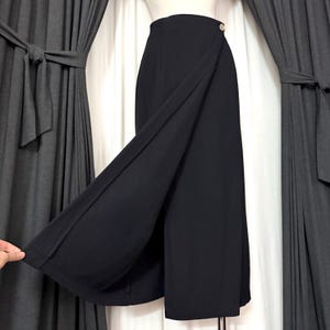 May include: Black wrap skirt with a button closure. The skirt has a high waist and a flowing design. The fabric appears to be a lightweight material. The skirt is shown against a neutral background.