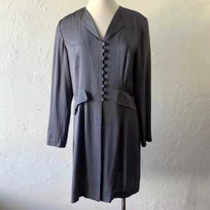 May include: A long-sleeved, gray dress with a button-up front and a v-neck. The dress has a fitted waist and a slightly flared skirt.