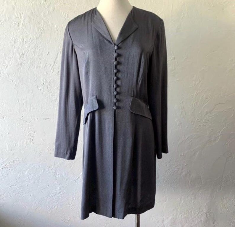 May include: A long-sleeved, gray dress with a button-up front and a v-neck. The dress has a fitted waist and a slightly flared skirt.