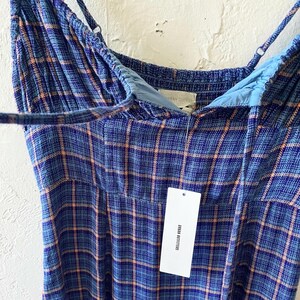 Puede incluir: Un vestido de cuadros azules y naranjas con tirantes finos. El vestido tiene una etiqueta que dice "Urban Outfitters".