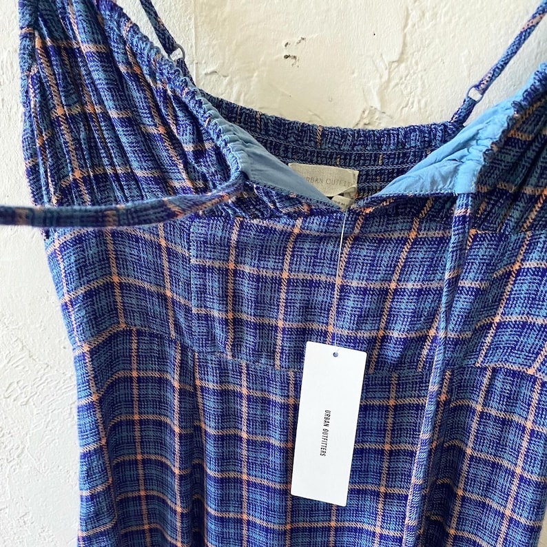 Puede incluir: Un vestido de cuadros azules y naranjas con tirantes finos. El vestido tiene una etiqueta que dice "Urban Outfitters".