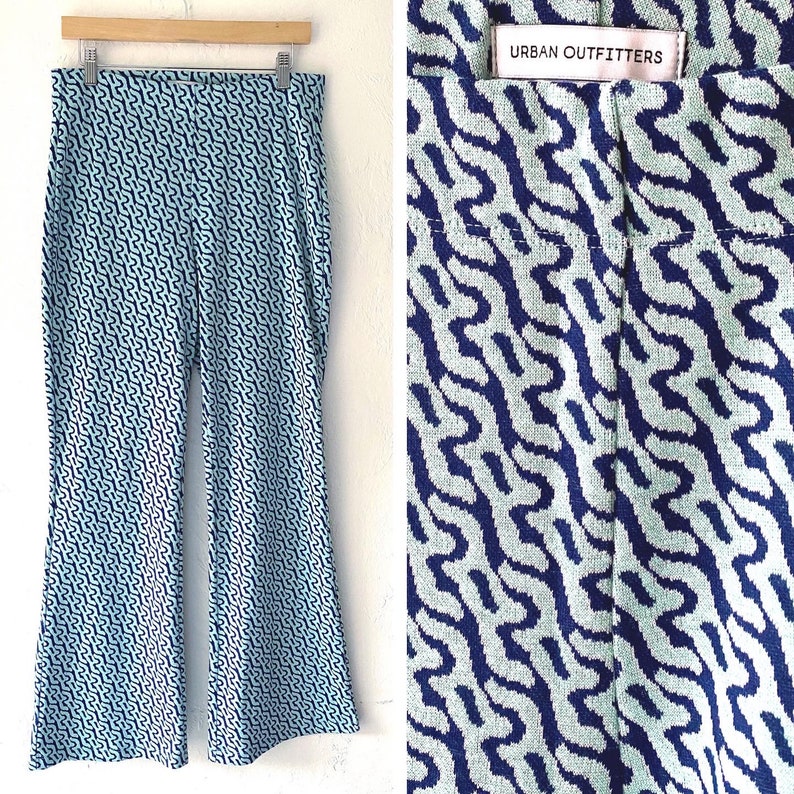 Puede incluir: Pantalones estampados en azul claro y azul marino colgados de una percha de madera. Los pantalones tienen una pernera acampanada y un dise&ntilde;o ondulado repetitivo. La etiqueta dice "Urban Outfitters".