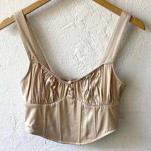 May include: A beige crop top with a sweetheart neckline and a button closure. The top has a fitted bodice and a ruffled neckline.