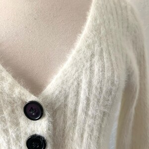 Peut inclure: Un cardigan blanc en fourrure avec un col en V et des boutons noirs.